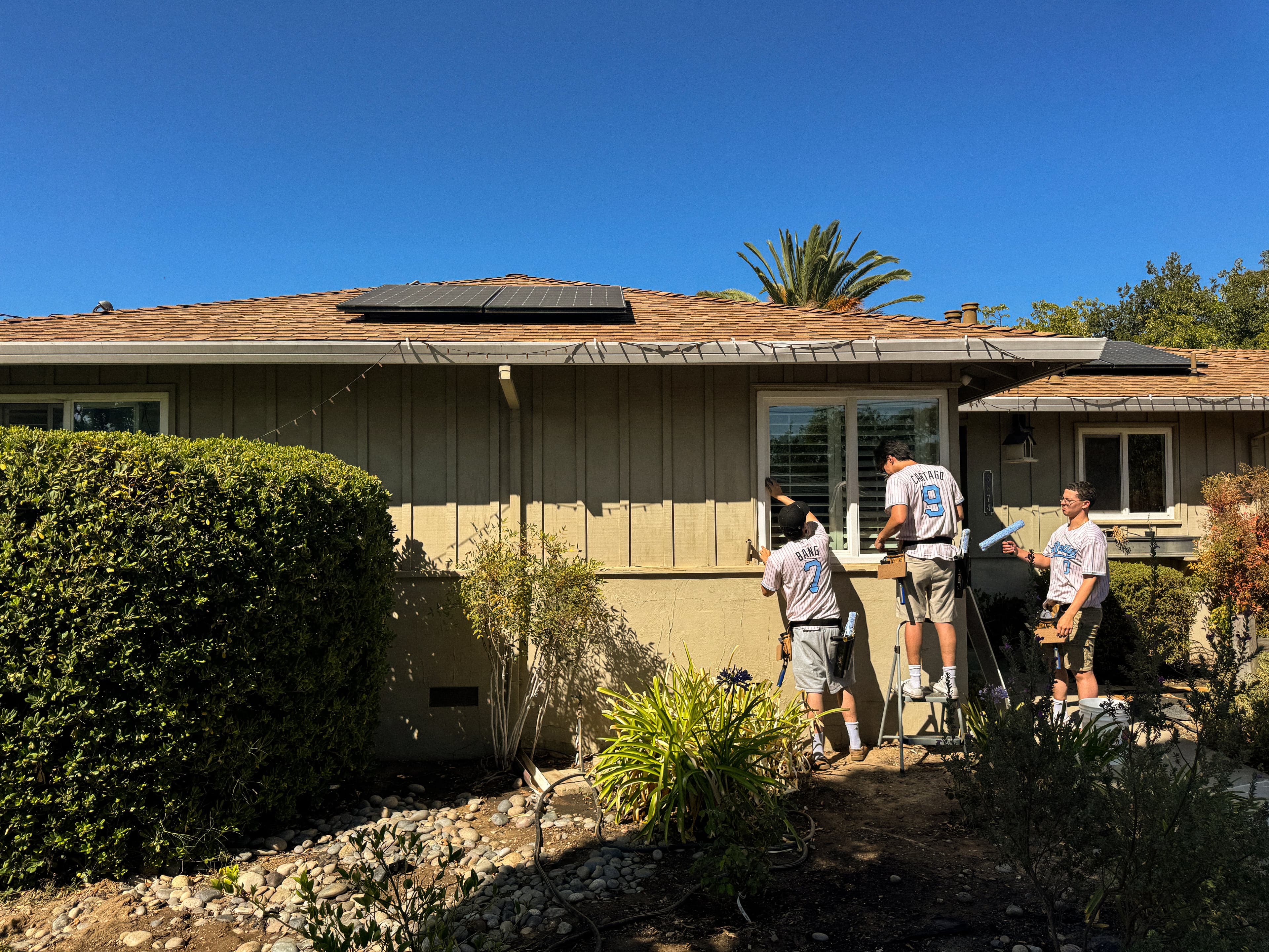 Three Rally cleaners in jerseys cleaning the front windows of a single-story home, one working from a step stool.